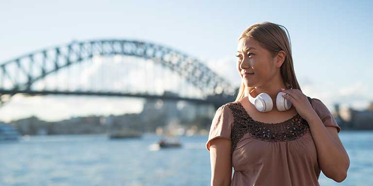 Woman in Sydney wearing headphones. Sydney Harbour Bridge is in the background